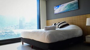 Een moderne hotelkamer met een groot bed, uitzicht over de stad en een schilderij aan de muur.