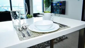 Ett modernt matbord med vita tallrikar, ett glas och bestick, och utsikt över staden genom stora fönster.