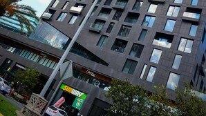 En modern skyskrapa med en fasad som har ett rutmönster, en Subway-restaurang på bottenvåningen och en klar himmel i bakgrunden.