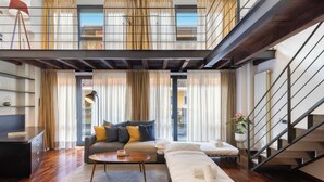 A modern living room with a sofa, a coffee table, and a bed. There is a staircase to the right and a balcony with curtains. - Loft Bandiello by BarbarHouse (Milano)