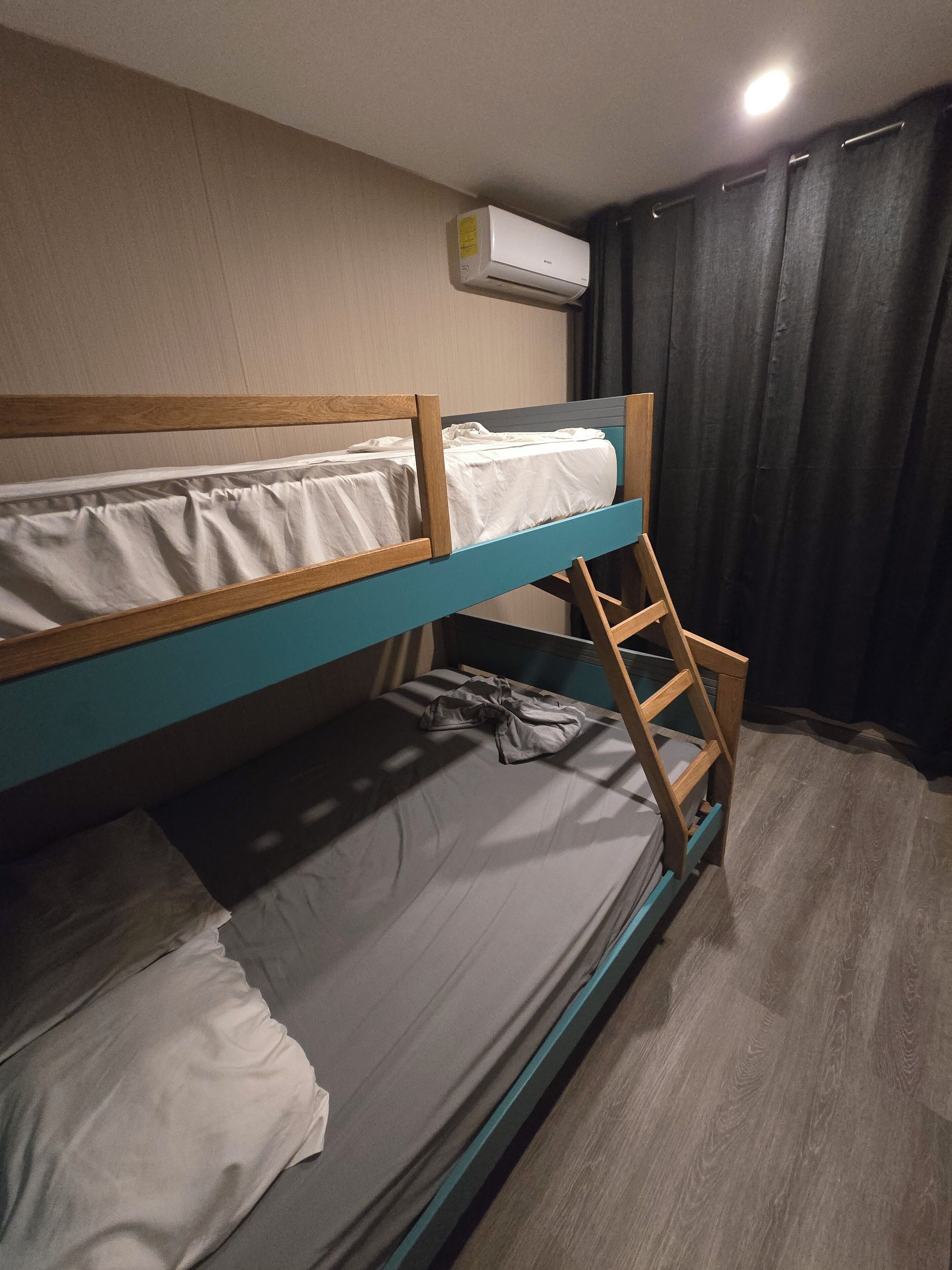 Dormitorio con literas, una escalera, aire acondicionado instalado en el techo y una cortina.