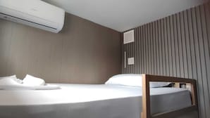 Una cama individual con ropa de cama blanca y un cabecero de madera, una unidad de aire acondicionado arriba y una pared de listones a la derecha.