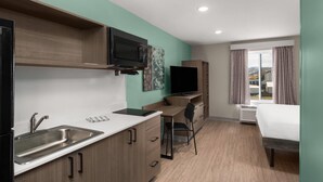 A compact hotel room with a kitchenette, a flat-screen TV, a bed, and a window with curtains. - Echo Suites Extended Stay By Wyndham Bozeman (Bozeman)