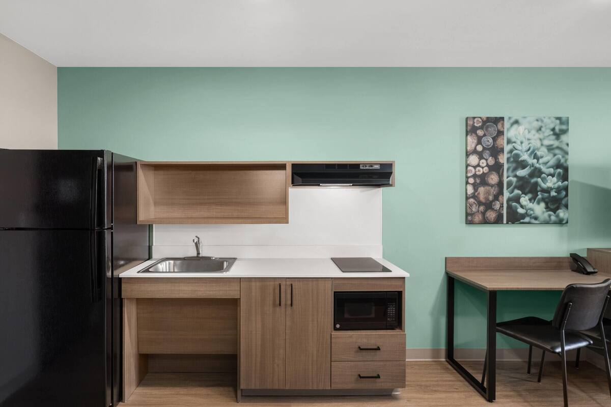Una cocina compacta con un refrigerador negro, armarios de madera, un microondas y un lavamanos pequeño.