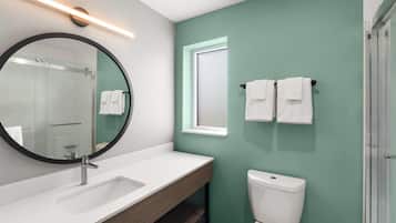 A bathroom with a white sink, a round mirror, a toilet, and a shower area.