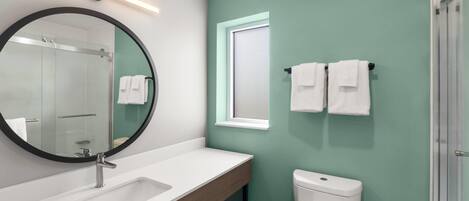 A bathroom with a white sink, a round mirror, a toilet, and a shower area.
