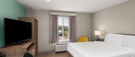 Ein Hotelzimmer mit Bett, Schreibtisch mit Fernseher, Sessel, Lampe und Fenster mit Vorhängen.