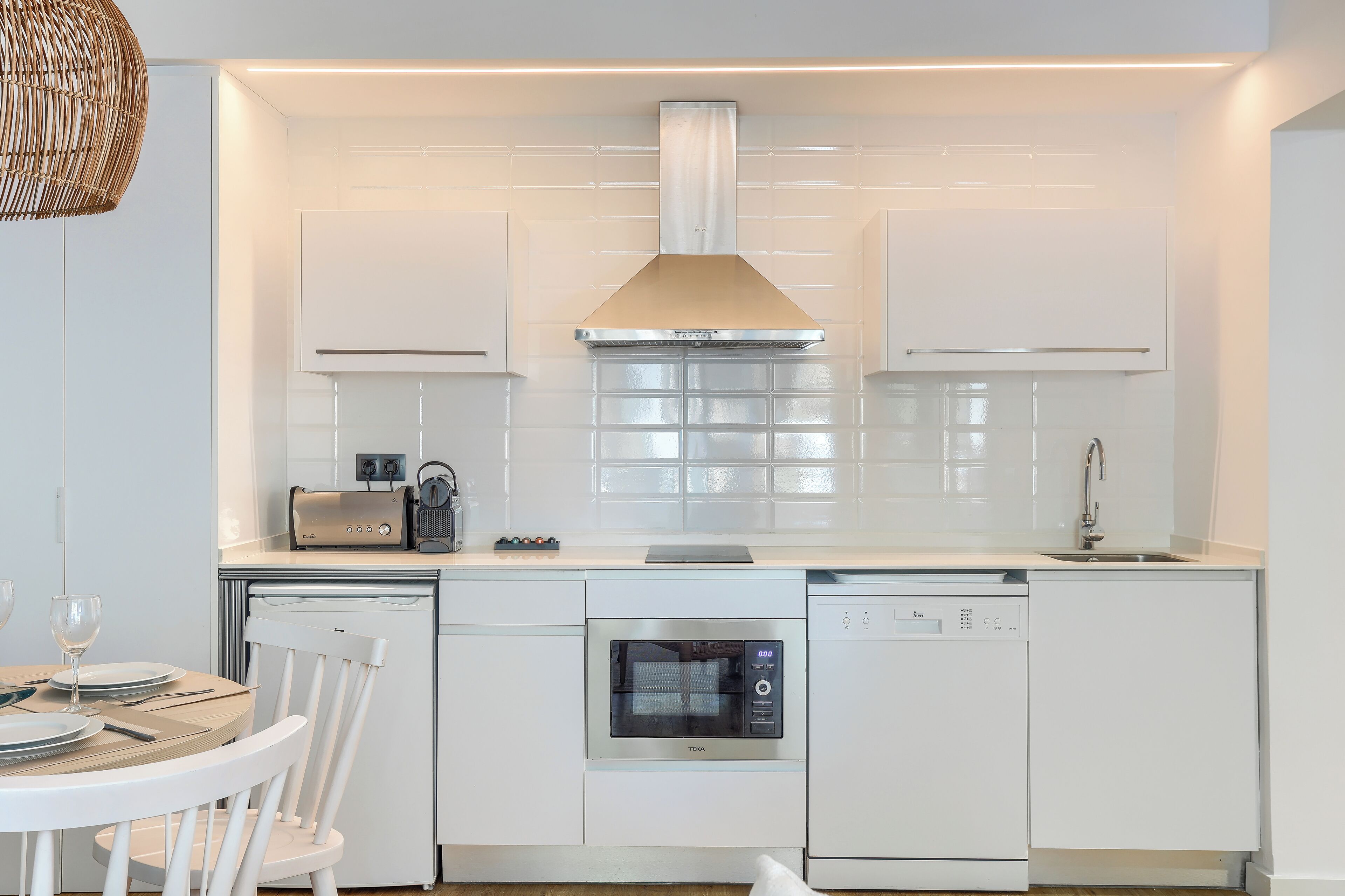 Une cuisine moderne avec des meubles blancs, un four encastré, un lave-vaisselle et un grille-pain.