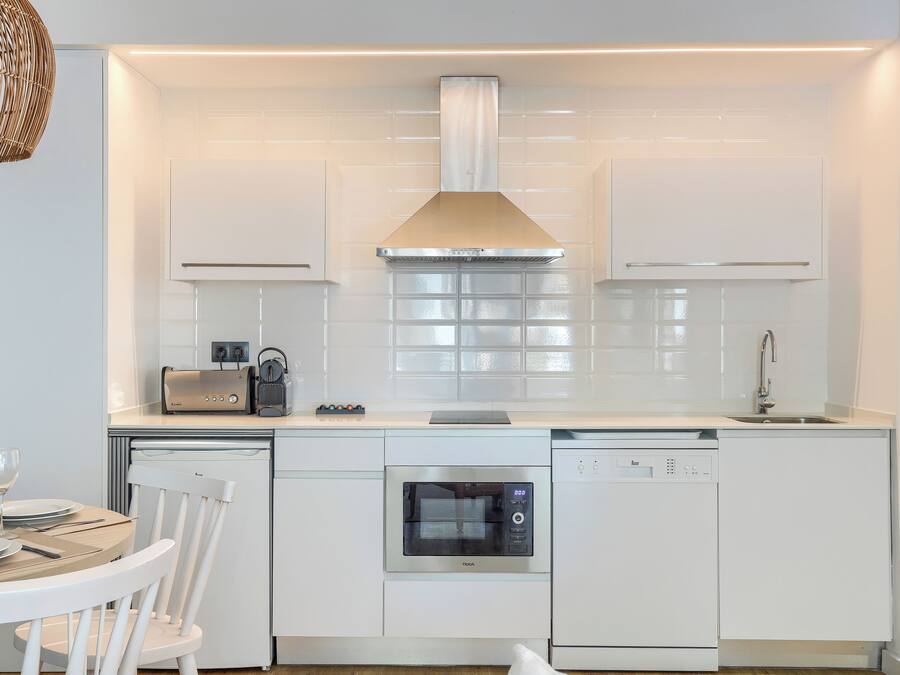 Une cuisine moderne avec des meubles blancs, un four encastré, un lave-vaisselle et un grille-pain.