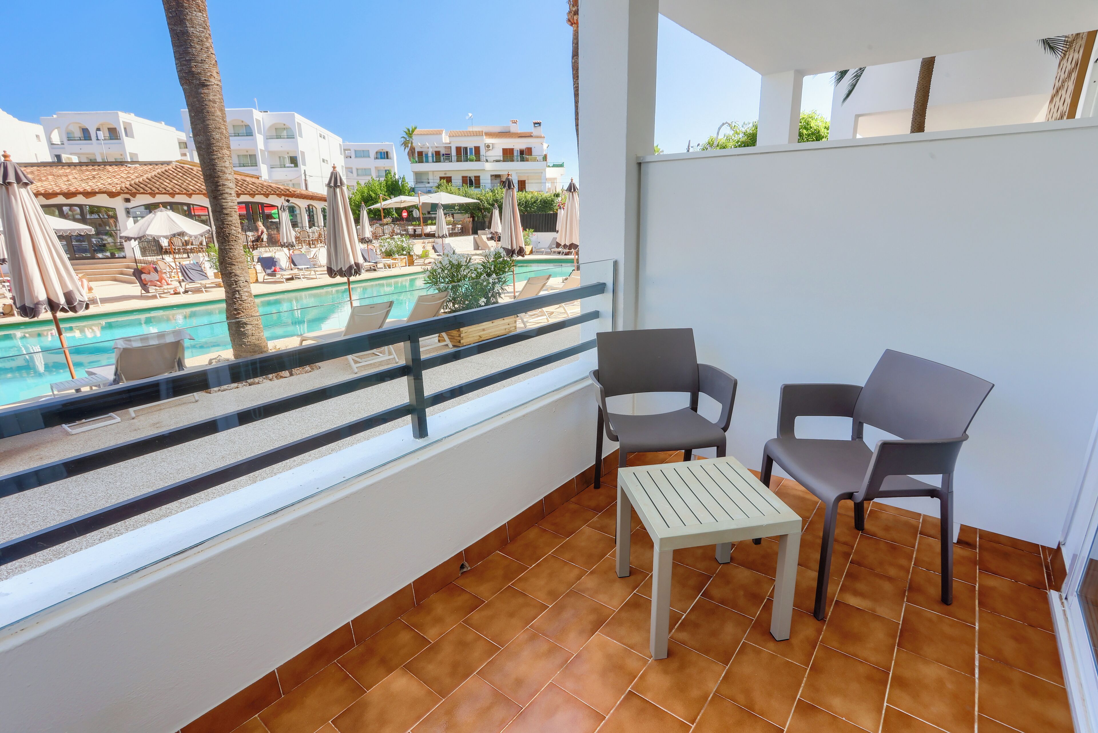 A balcony with a view of a pool, two chairs, and a small table.