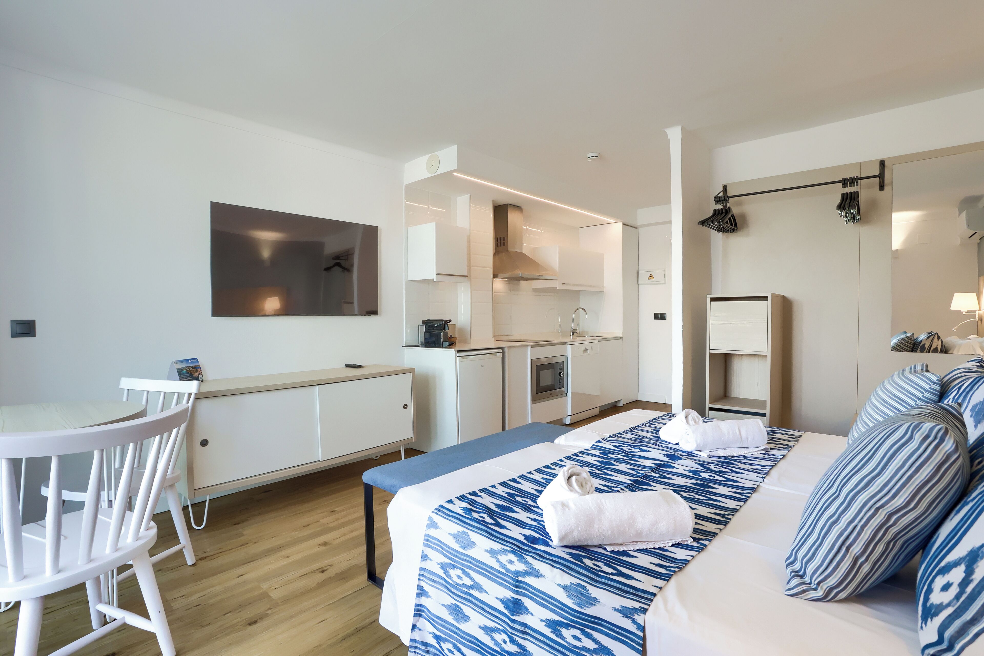 Una habitación de hotel moderna con cama, una pequeña cocina, una zona de comedor y un espejo grande.
