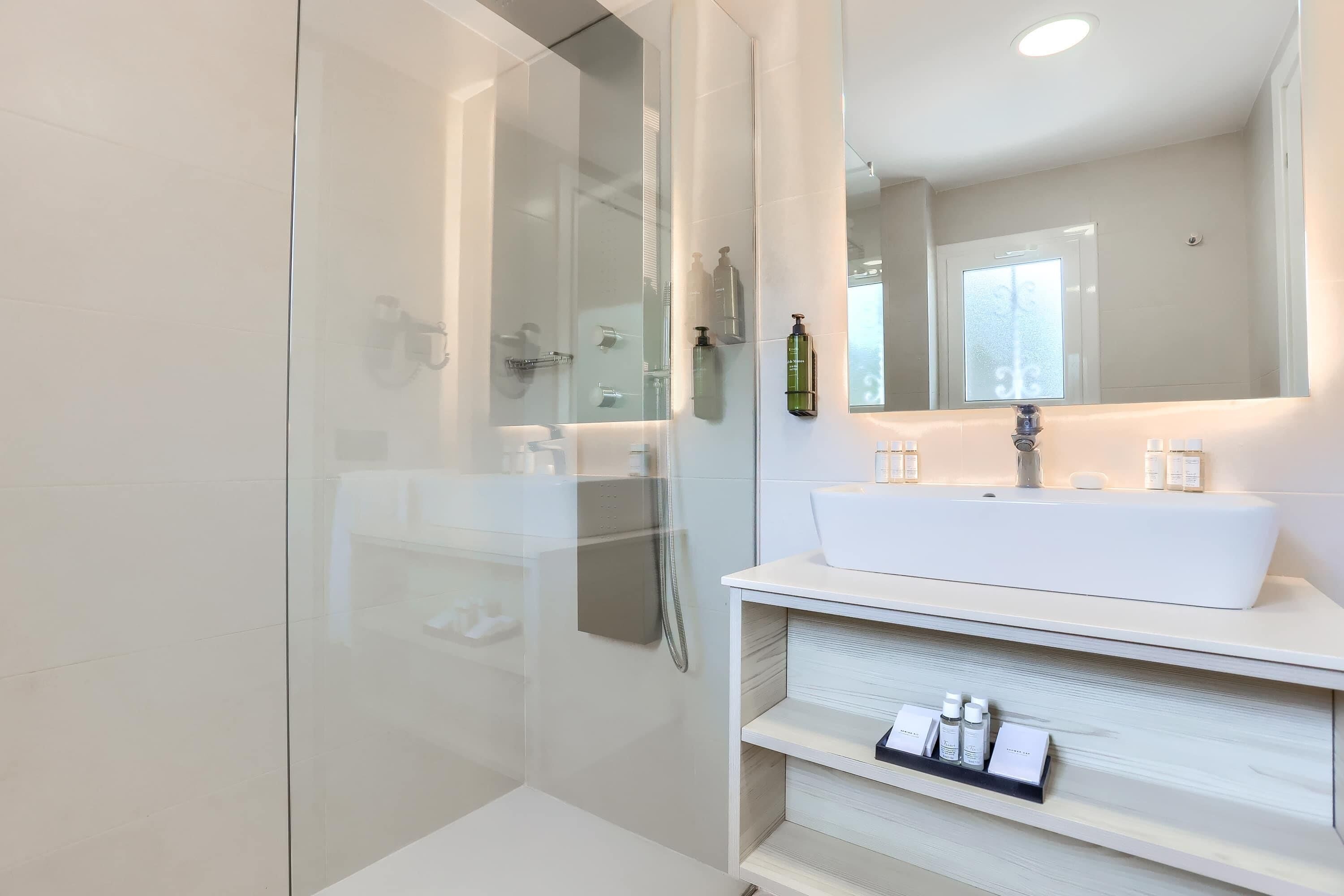 Un baño moderno con cabina de ducha de vidrio, un lavabo blanco y un espejo sobre él.