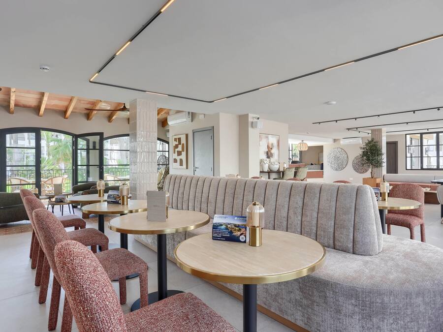 A modern hotel lobby with round tables, cushioned seating, and large windows.