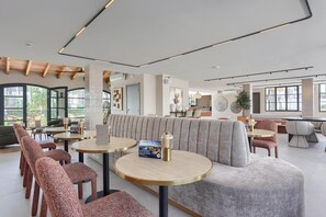Eine moderne Hotelhalle mit runden Tischen, gepolsterten Sitzgelegenheiten und großen Fenstern.