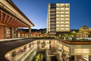 A modern hotel with a traditional architectural style, featuring a spacious lobby with a central water feature, a high-rise building with illuminated panels, and a well-lit outdoor area with seating. - Wyndham Grand Tengchong Hot Spring (Baoshan)
