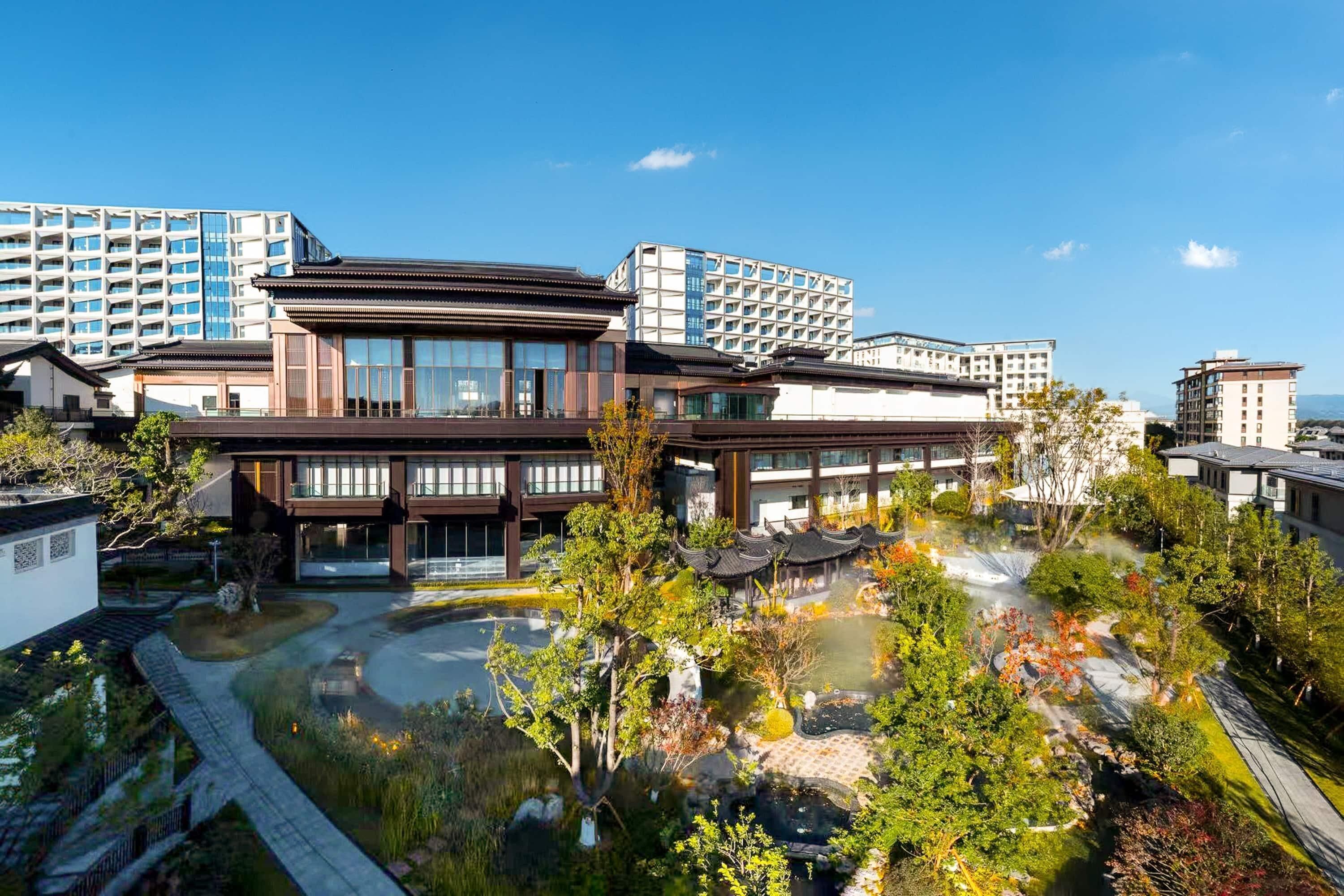 Un hotel moderno con elementos arquitectónicos tradicionales, un patio ajardinado y edificios altos circundantes.