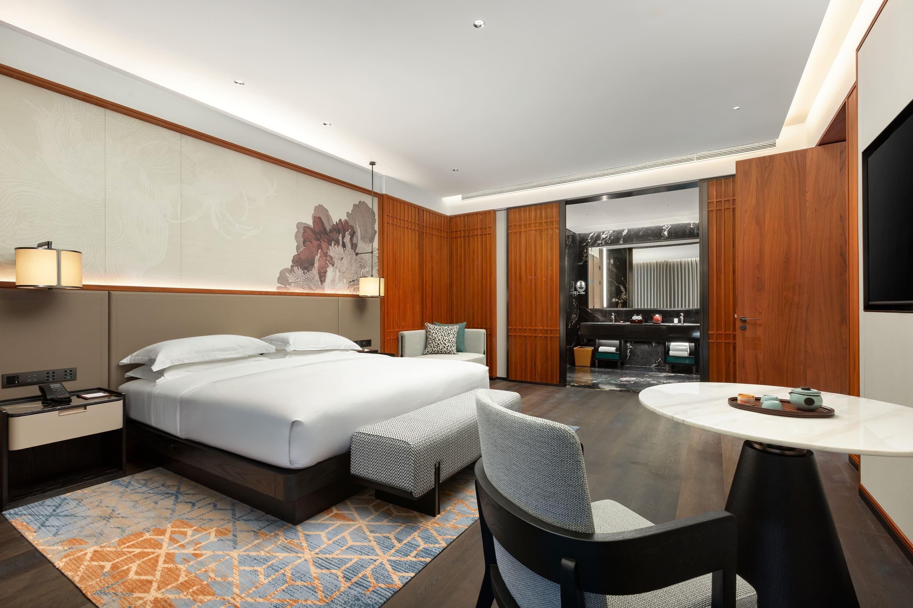 Une chambre d’hôtel moderne avec un grand lit, un bureau, une chaise, une petite table et un grand miroir.