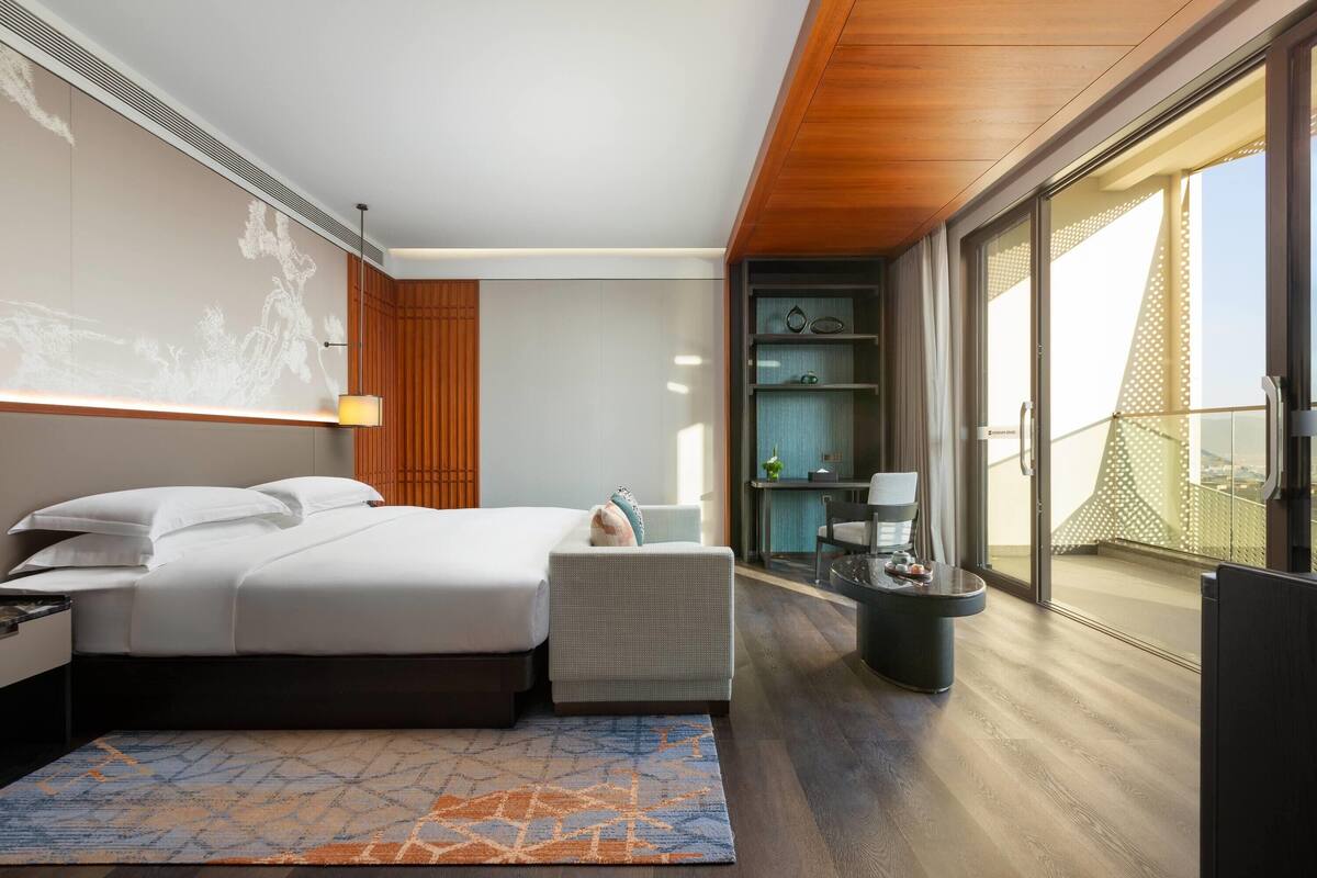 Habitación de hotel moderna con una cama grande, una zona de estar pequeña, un balcón con vistas y un minibar.