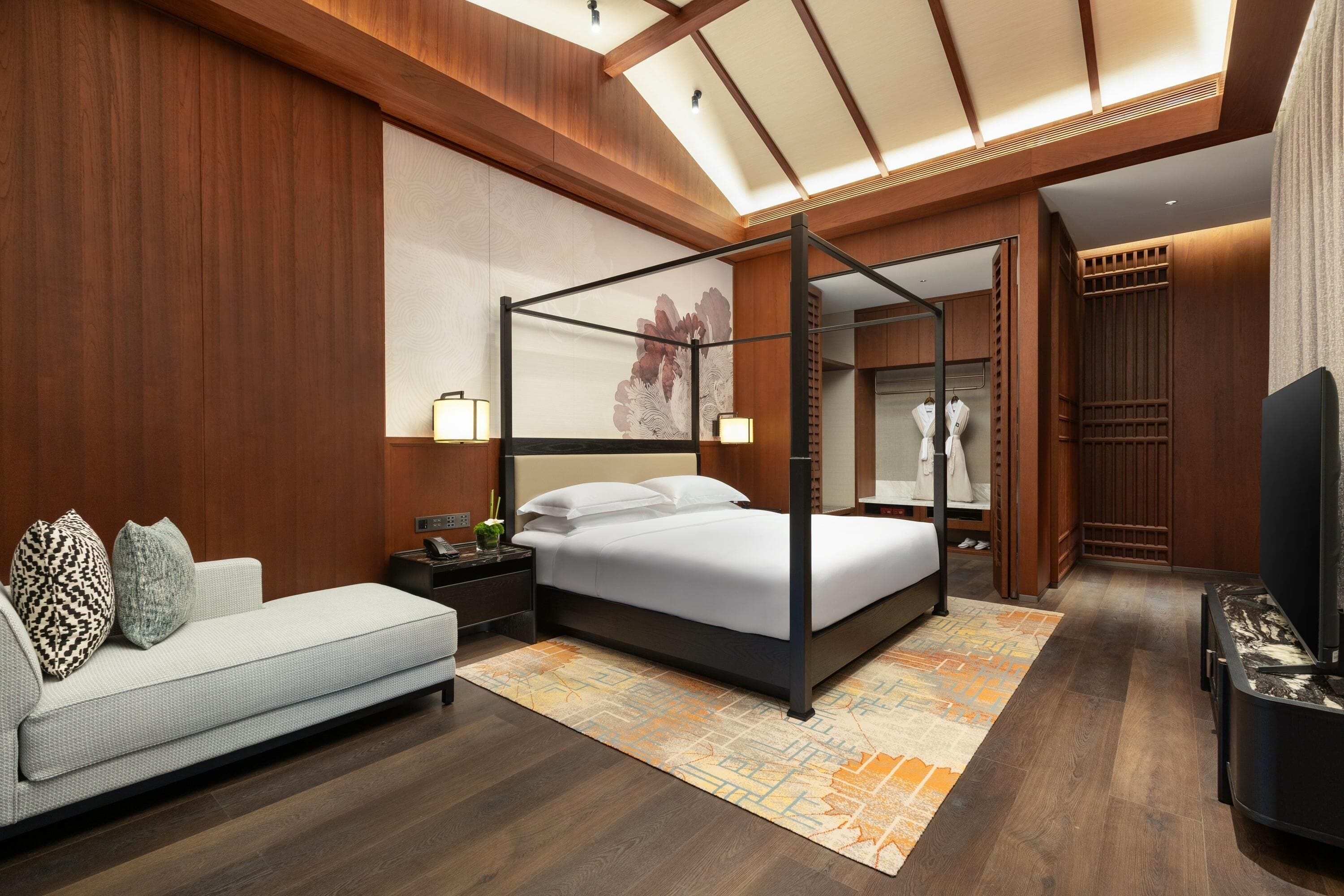 A modern bedroom with a four-poster bed, a sofa, and a TV.