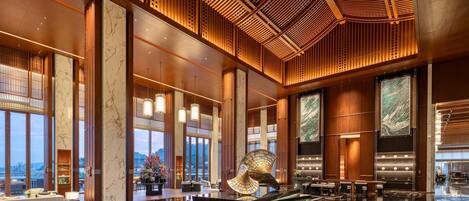 A spacious lobby with a polished marble floor, large wooden columns, and a high ceiling with intricate woodwork.