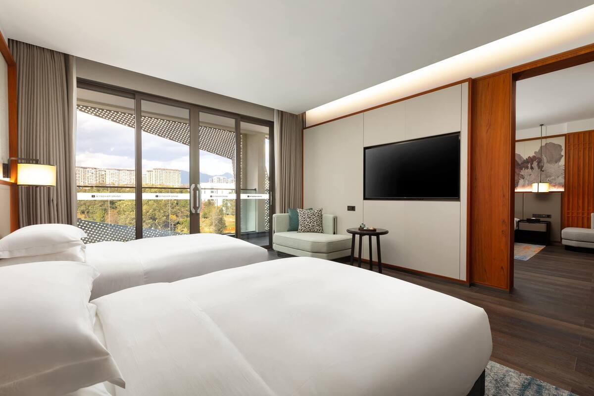 Habitación de hotel con dos camas, televisión, sofá y vista a la ciudad.