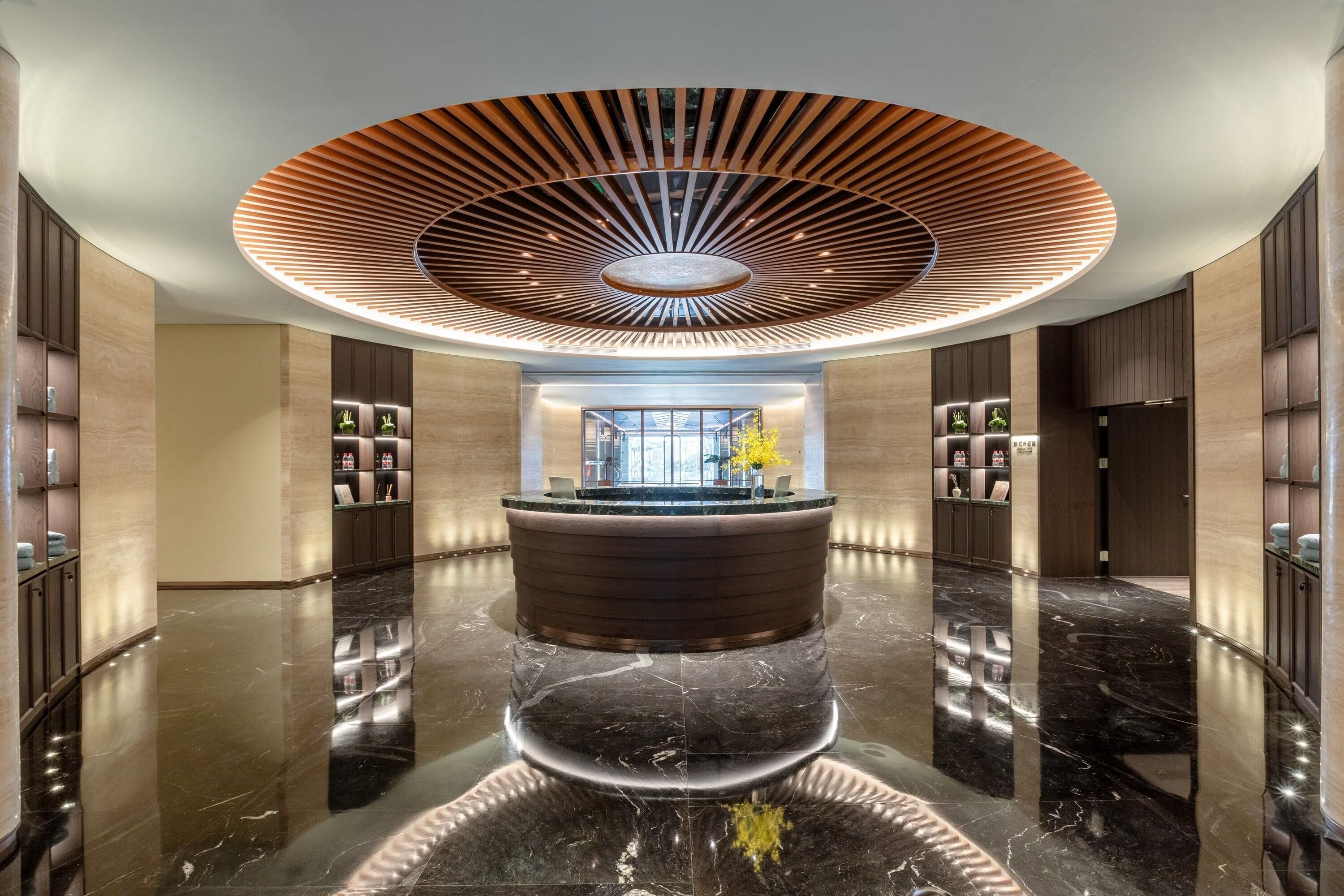 A modern lobby with a central reception desk, a polished marble floor, and a unique ceiling design.