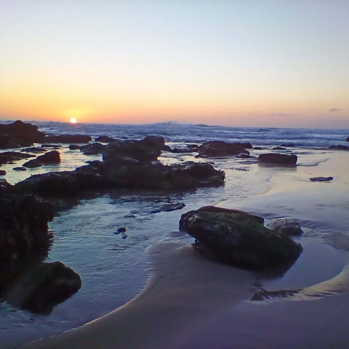 Una spiaggia al tramonto con rocce e acqua.