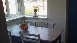 A dining area with a table and chairs, a window with a view of a rocky landscape, and a small potted plant on the windowsill. - Fabulous position a sandy beach and stunning coastal walks. Family friendly. (Truro)
