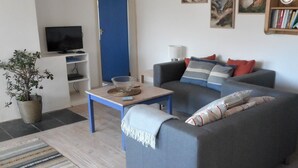 A living room with a grey sofa, a coffee table, a TV, and a bookshelf. - Fabulous position a sandy beach and stunning coastal walks. Family friendly. (Truro)