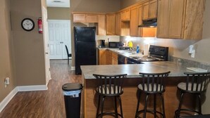 A kitchen with wooden cabinets, a black refrigerator, a stove, and a bar area with stools.