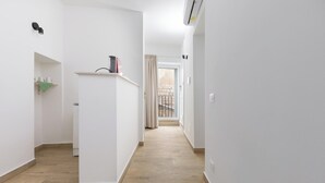 Kapea käytävä, jossa on puulattia, valkoiset seinät ja ovi, joka johtaa ulkotilaan.