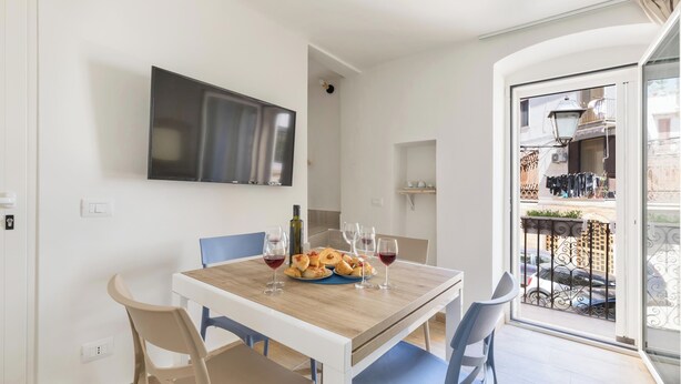 Ein Essbereich mit Holztisch, Stühlen, einem Flachbildfernseher und einem Balkon mit Geländer.
