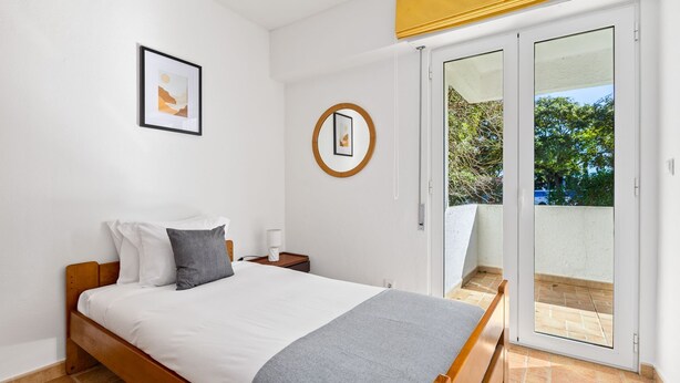 Een slaapkamer met een bed, een nachtkastje, een ingelijste foto aan de muur en een schuifdeur die leidt naar een buitenruimte.