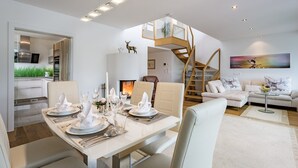 A modern dining area with a white table set for four, a staircase leading to an upper level, and a living room with a sofa and a painting. - Luxury Apartment Silvia, Lake view & Terrace (Zell am See)