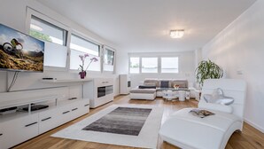 A modern living room with a flat-screen TV, a sofa set, a coffee table, and a large window. - Luxury Apartment Silvia, Lake view & Terrace (Zell am See)
