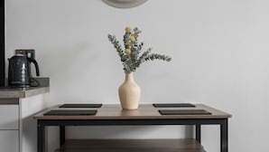 Et køkken med et ur, en kaffemaskine, en vase med blomster og et bord med servietter.
