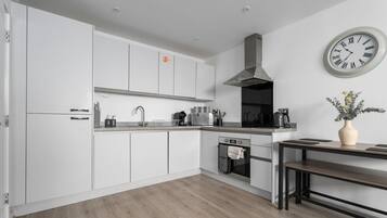 A modern kitchen with white cabinetry, a stainless steel range hood, a built-in oven, a sink, and a clock on the wall.