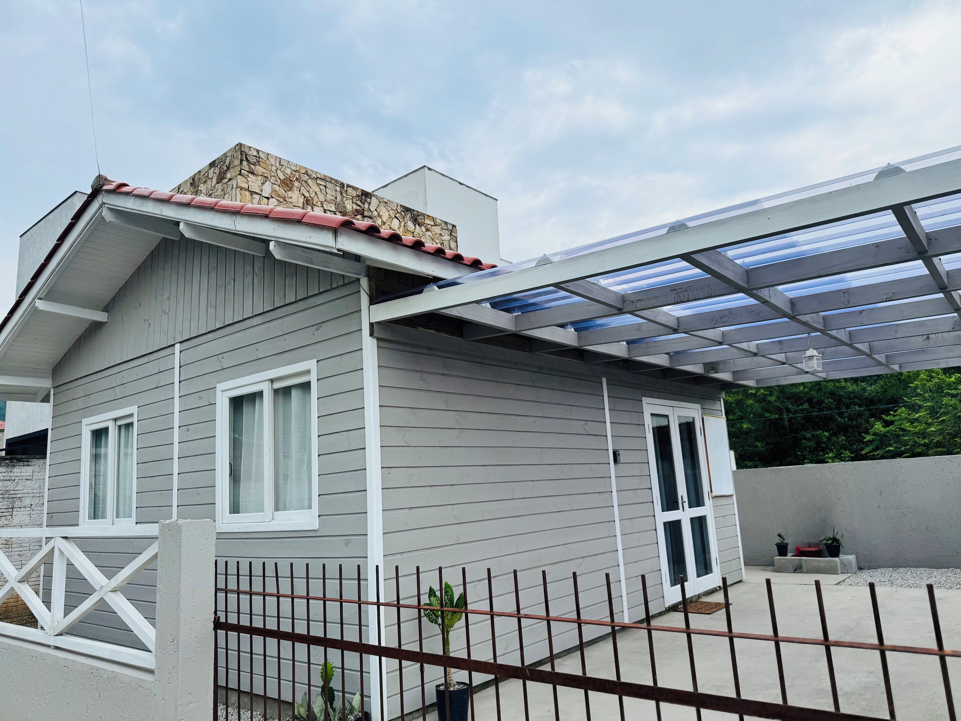 Una casa con fachada gris, detalles blancos, techo de tejas rojas y un porche cubierto con techo de metal.