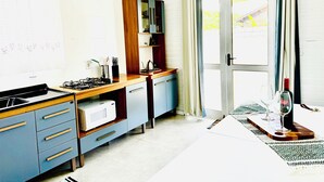 Une cuisine équipée d’une cuisinière à gaz, d’un four à micro-ondes et de placards. Il y a une fenêtre avec des rideaux et une porte donnant sur l’extérieur.