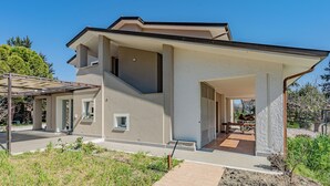 Una moderna casa a due piani con patio coperto, una scala visibile e un piccolo giardino.