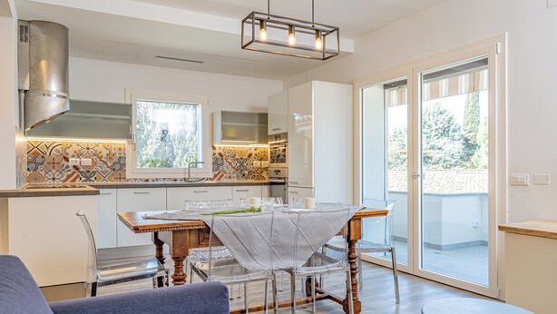 Una cucina moderna con zona pranzo, ampie finestre e una porta scorrevole in vetro che dà su un balcone.