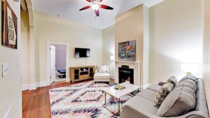 A living room with a sofa, coffee table, and a fireplace. There is a television mounted on the wall and a ceiling fan.