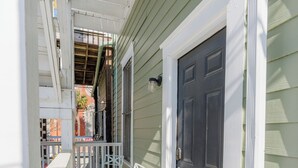 A narrow porch with a white railing, a dark door, and a white chair.