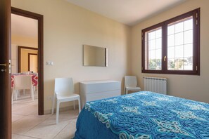 Una camera da letto con un letto, due sedie, una cassettiera, uno specchio e una finestra.