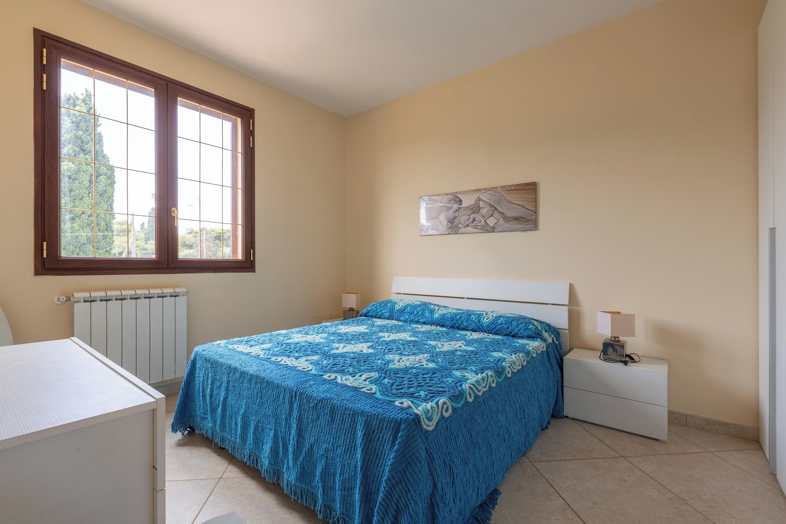 A bedroom with a bed, bedside table, lamp, and a window.