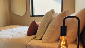 A bedroom with a bed, pillows, a bedside table, a lamp, and a window with a view of a building. - Luxury villa & carpark, retreat close to everything (Queenstown)