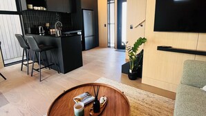 A modern living space with a round wooden coffee table, a kitchen area with black cabinetry, a flat-screen TV mounted on the wall, and a seating area with a grey sofa. - Luxury villa & carpark, retreat close to everything (Queenstown)