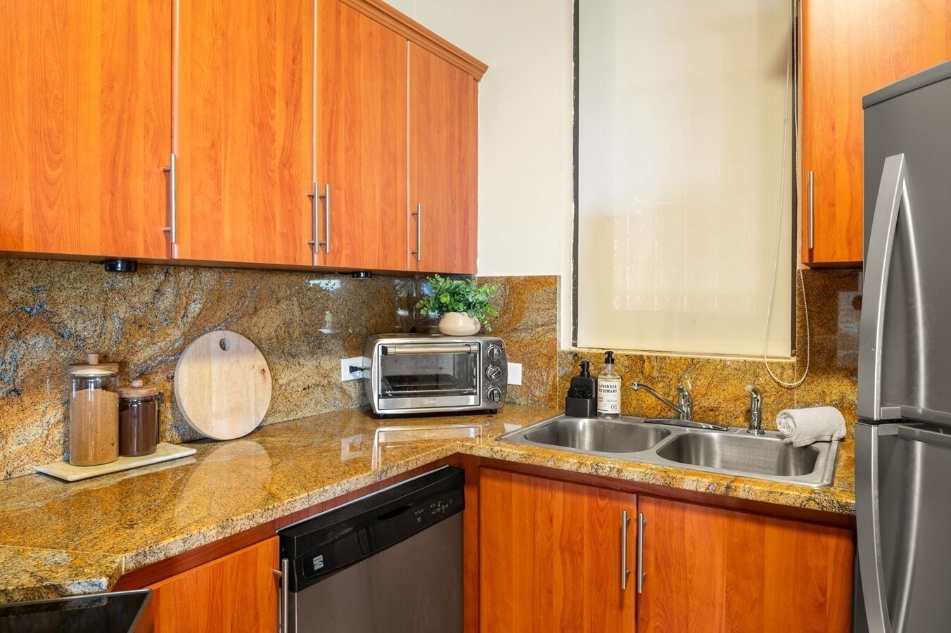 A kitchen with wooden cabinets, granite countertops, a toaster, a sink, and a dishwasher.