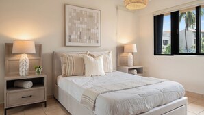 A bedroom with a large bed, two bedside tables with lamps, a wall-mounted artwork, and a window with a view of palm trees. - Crescent Beach by Otium (Humacao)