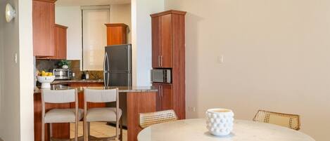 Een compacte keuken met houten kastjes, een koelkast, magnetron en een eethoek met een ronde tafel en stoelen.